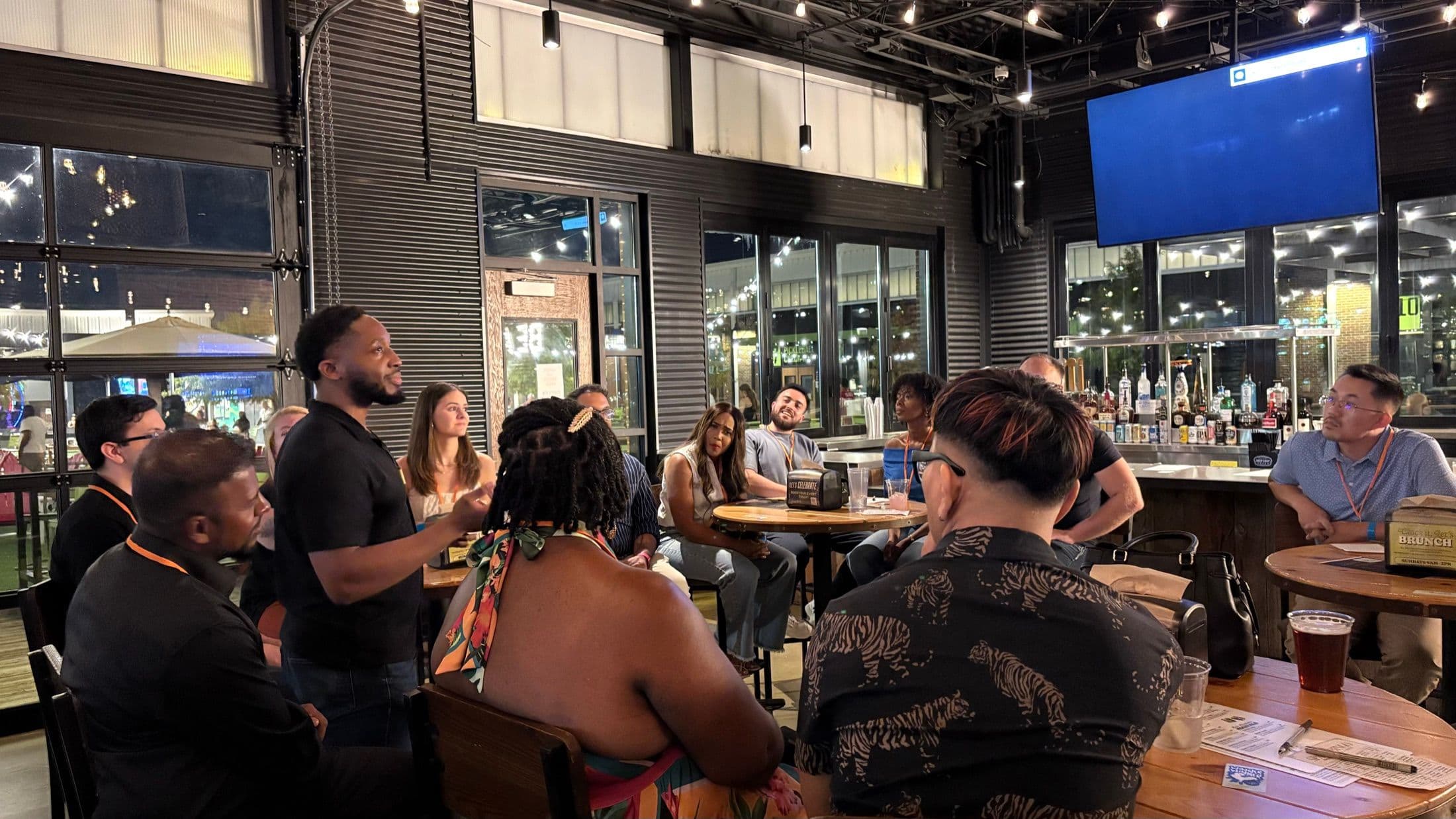 A Beyond The Sparks host speaking to guests at high-top tables during an evening dating event.