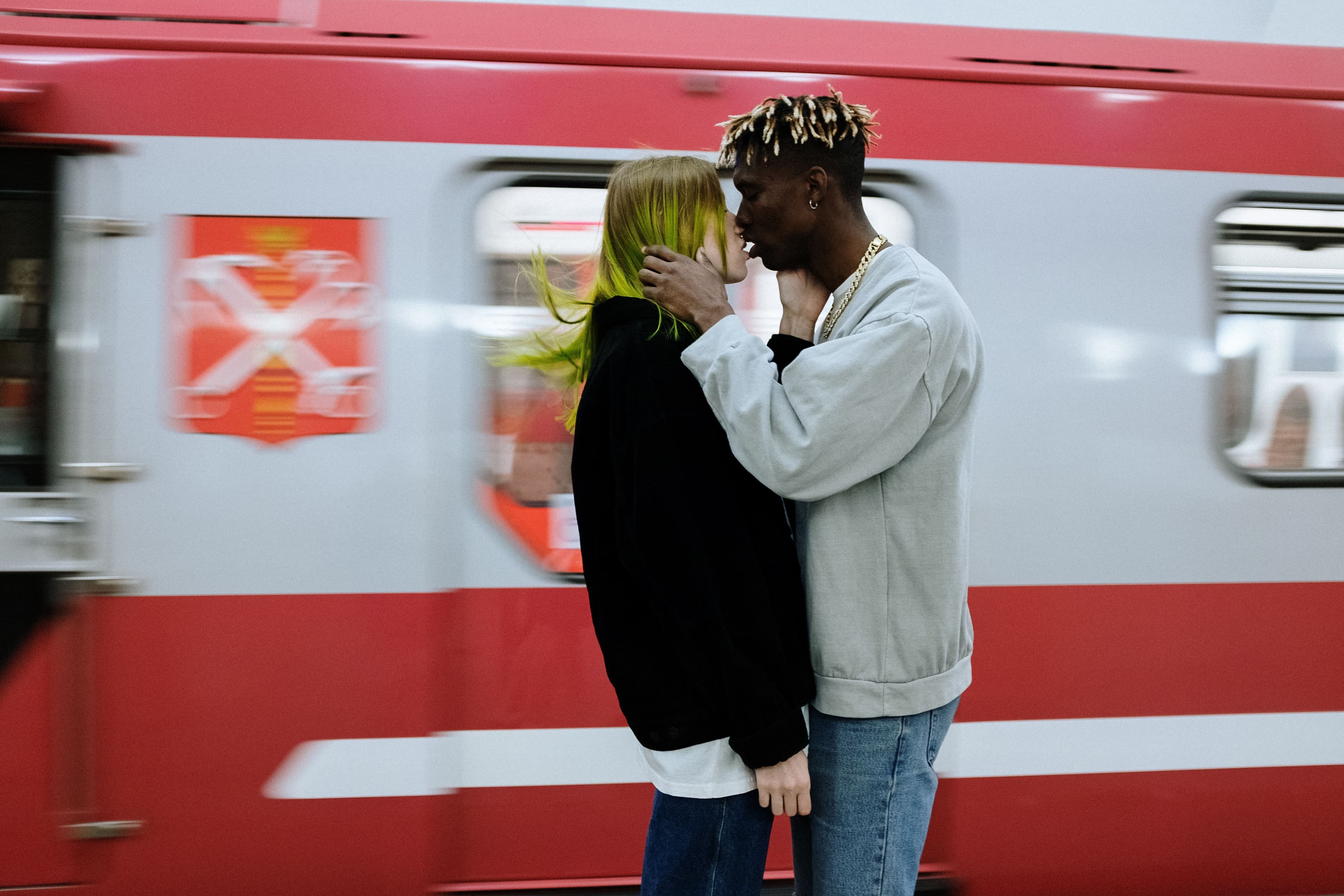 A young couple kissing passionately on a subway platform with a blurred train passing behind them, illustrating the intense rush of limerence and falling in love fast.