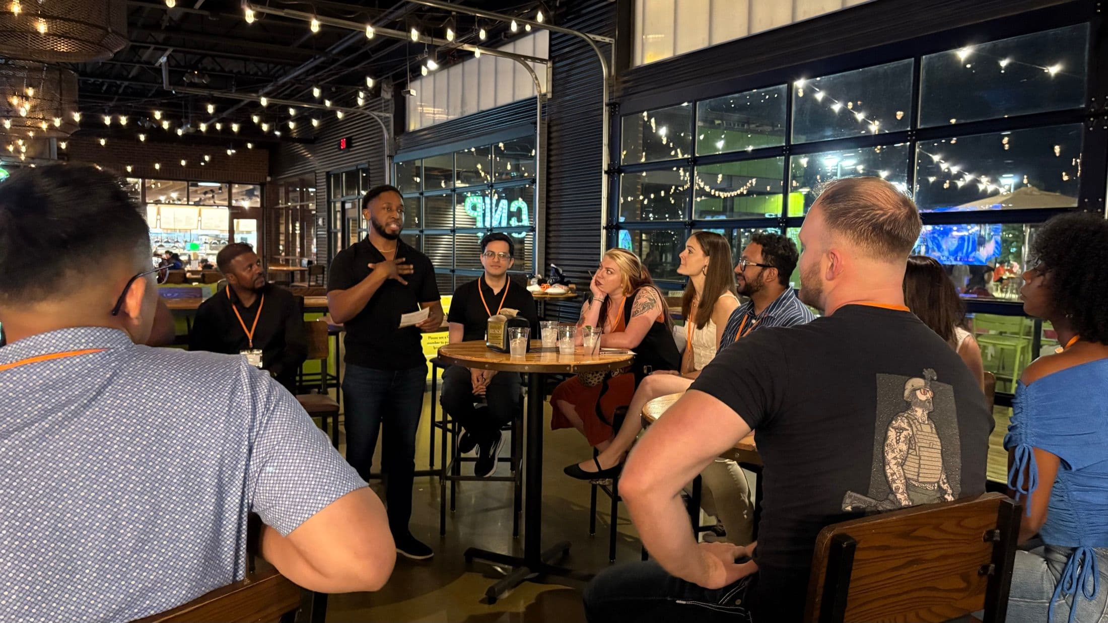A Beyond The Sparks host addressing seated guests under string lights at an evening dating event.