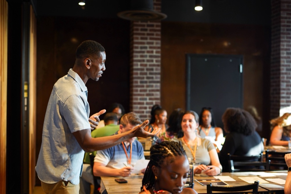 A Beyond The Sparks host speaking to seated guests at a compatibility dating event in a brick-walled venue.
